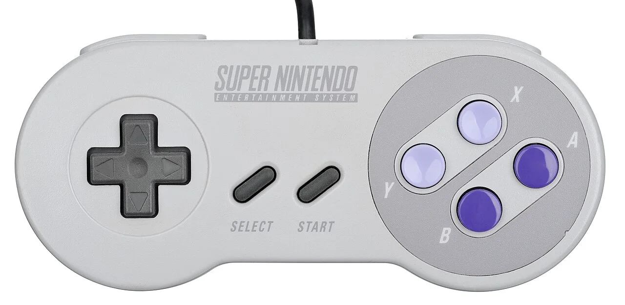 北美版 SNES 手柄正面。图为 Evan-Amos 摄 / Wikimedia Commons，公有领域。注意图中为北美版配色（X/Y 淡紫凹陷、A/B 紫色凸起），与日版/欧版四色按钮不同，属同款手柄的区域变体。