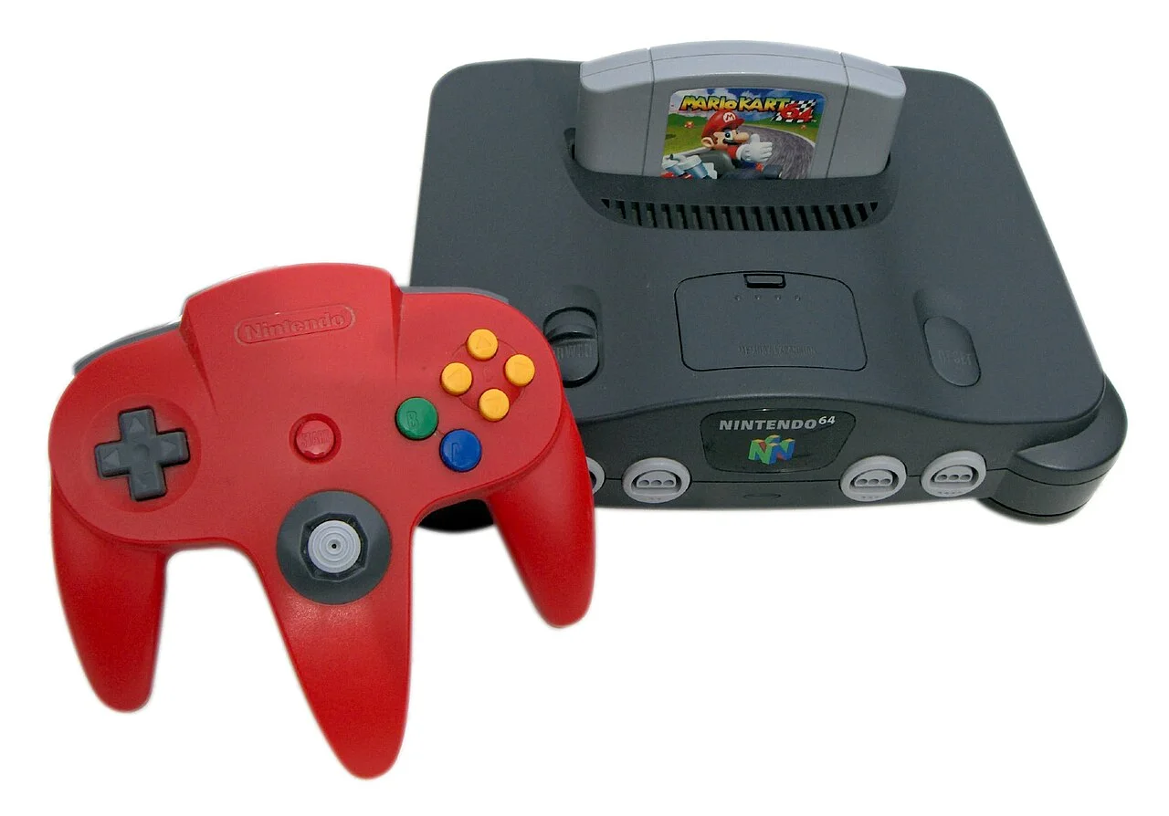 N64 主机插着日版《马力欧卡丁车64》卡带。图为 Céréales Killer 摄 / Wikimedia Commons，CC BY-SA 3.0。图为日版机器与日版卡带；区域锁定通过卡带背面的豁口形状实现，不同区域卡带物理上无法互插。