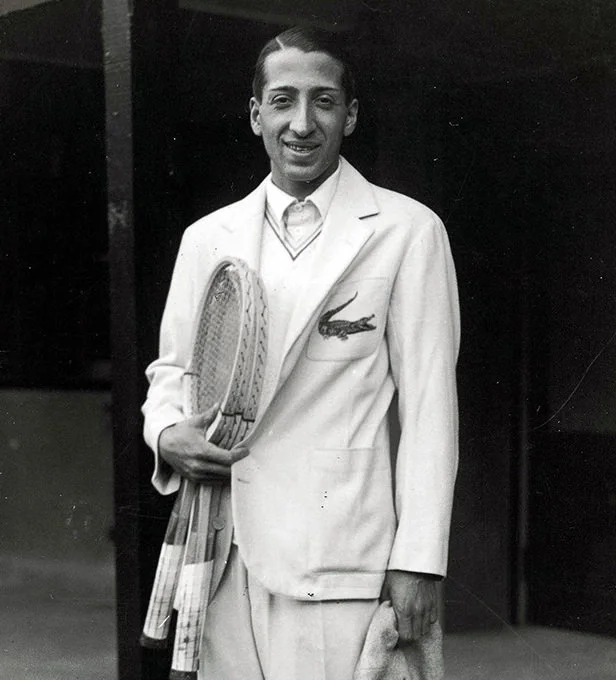 René Lacoste穿着绣有鳄鱼标识的白色西装(1920年代,Popperfoto)。这是鳄鱼成为他个人可穿戴标识的最早图像证据。 · 图像文件署名:Unknown, PHOTO © POPPERFOTO – GETTY;Public domain;网页缩放,原始文件保留。